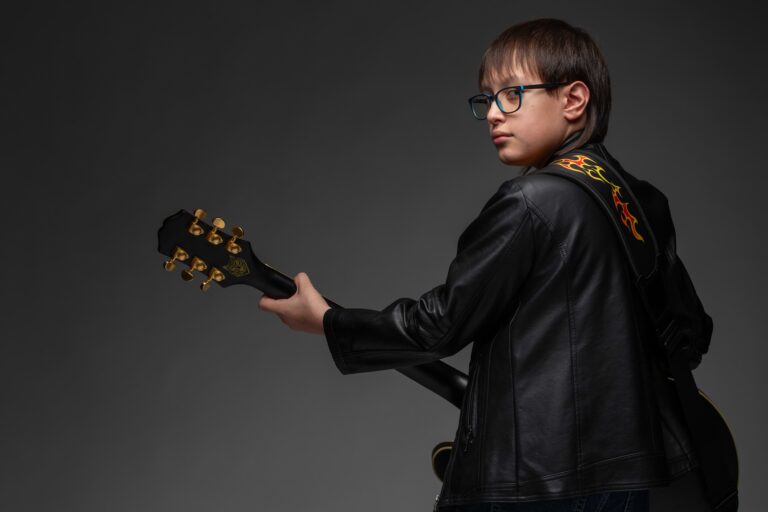 Holden Garcia wearing glasses and a black jacket, looking over his shoulder with an acoustic guitar.