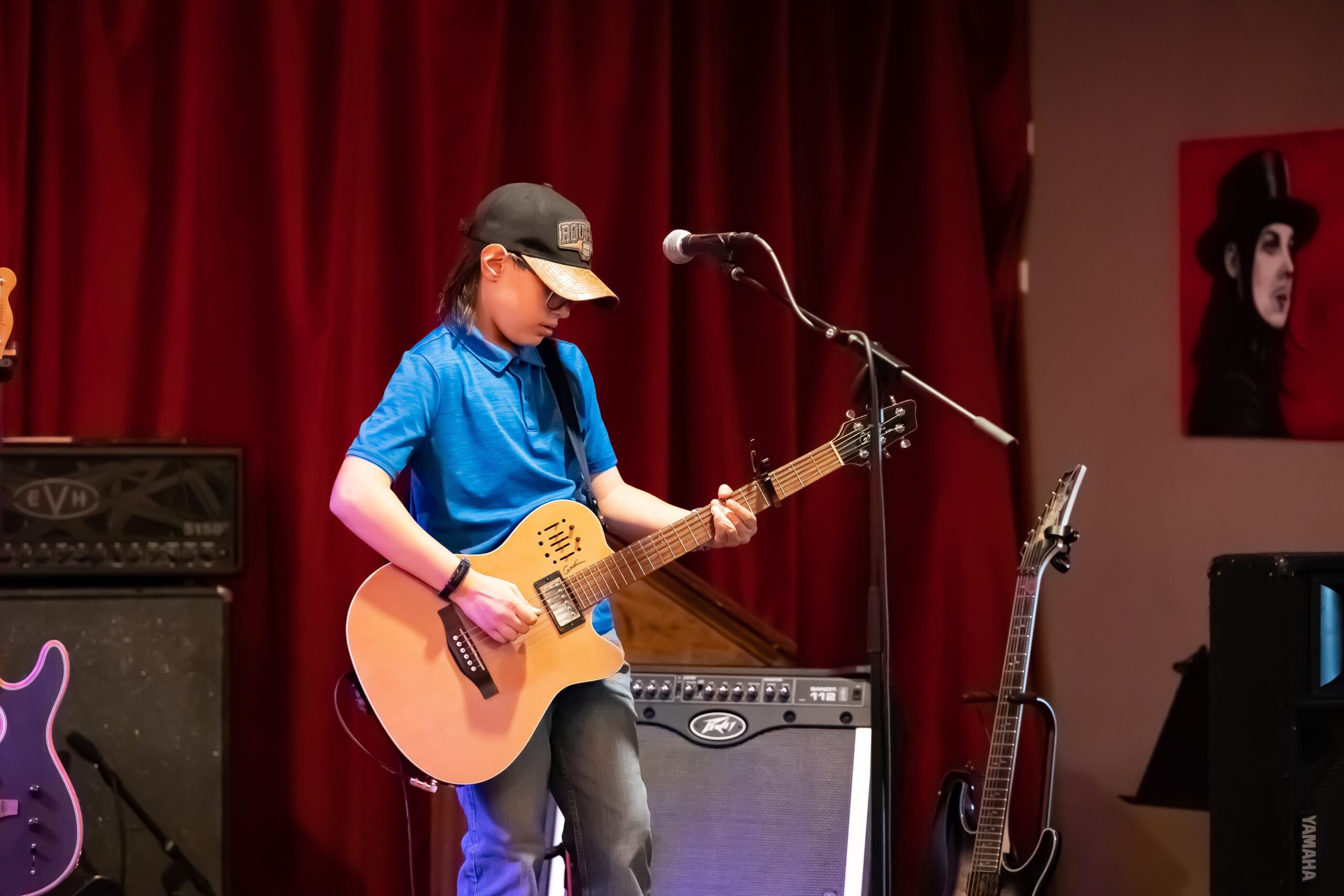 Holden Garcia playing acoustic guitar in front of a red stage curtain.